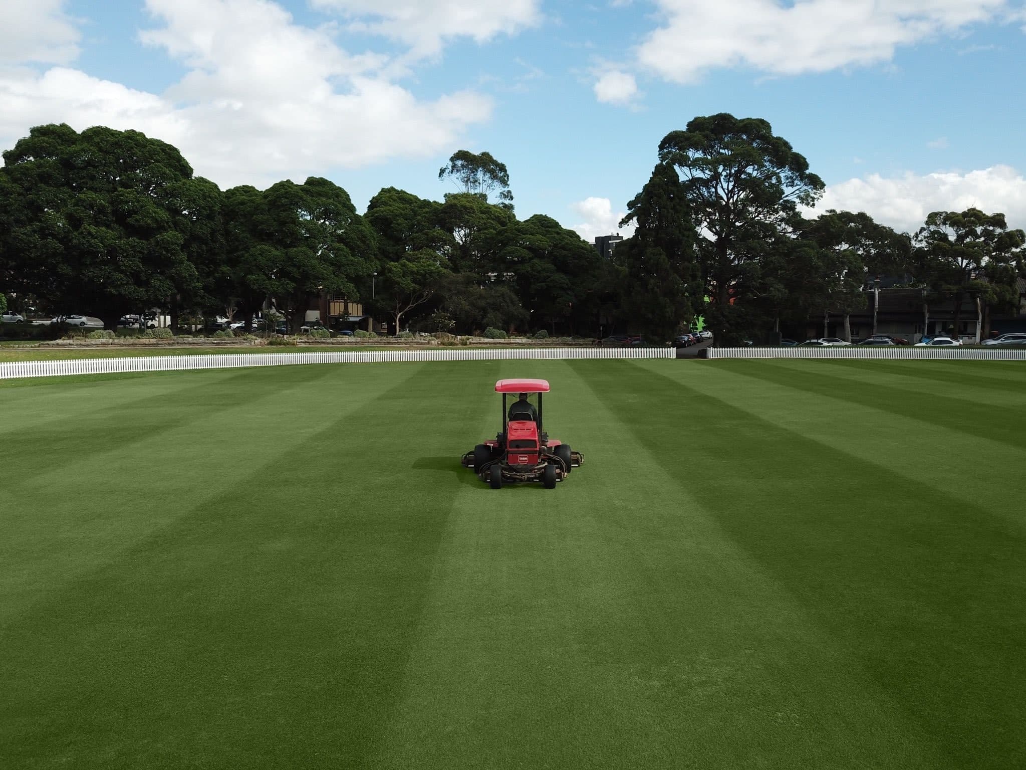 Ride-on mower leaving striped patterns on a large green field